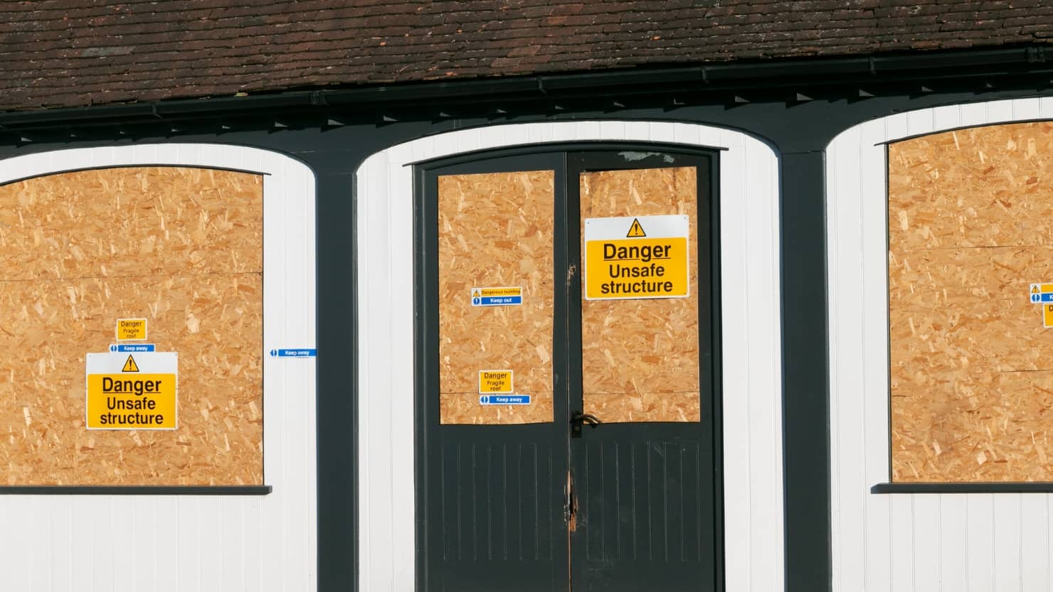 Property windows and doors boarded up for security, with a sign stating danger unsafe structure